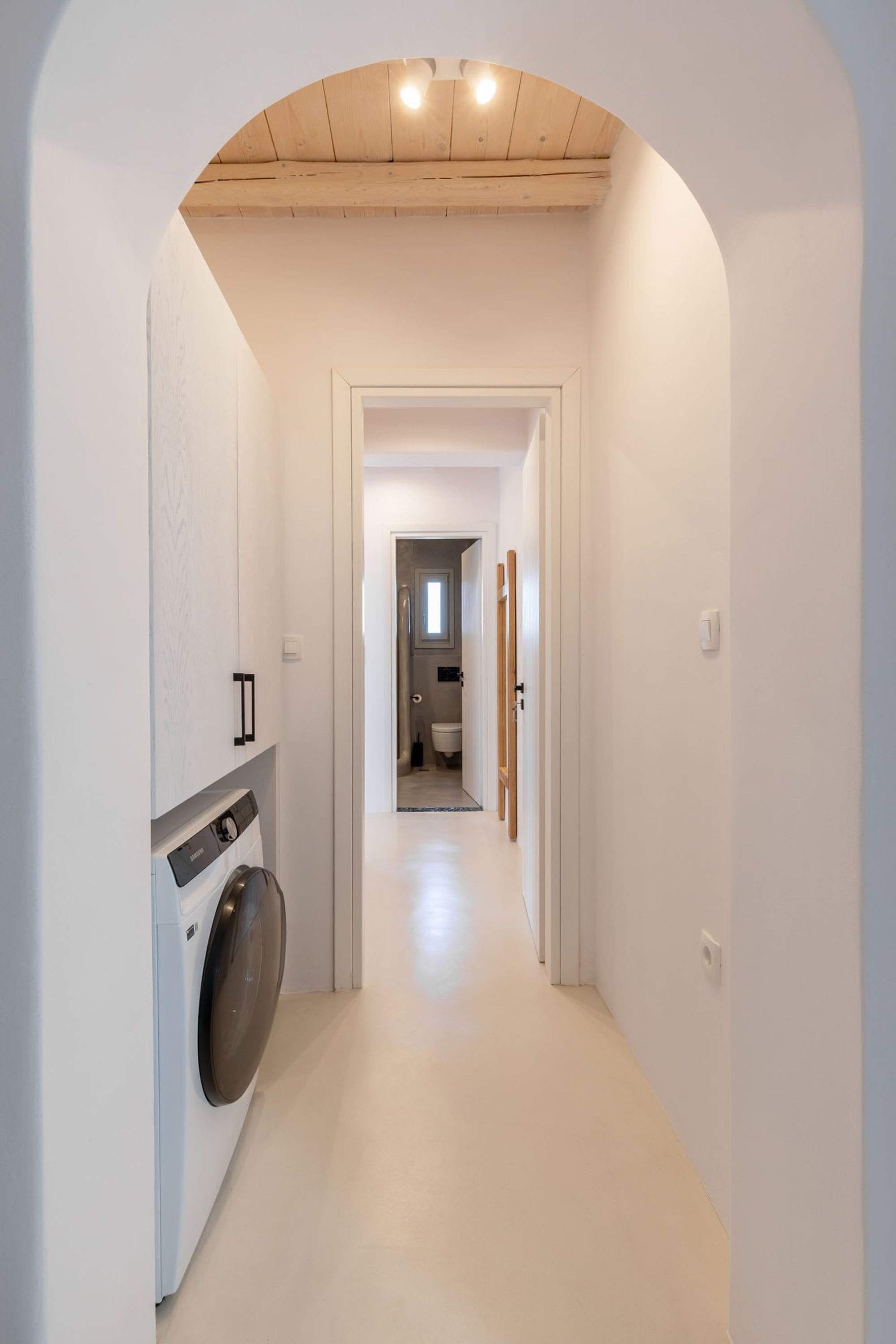 A narrow hallway with a washing machine on the left, leading to a bathroom.