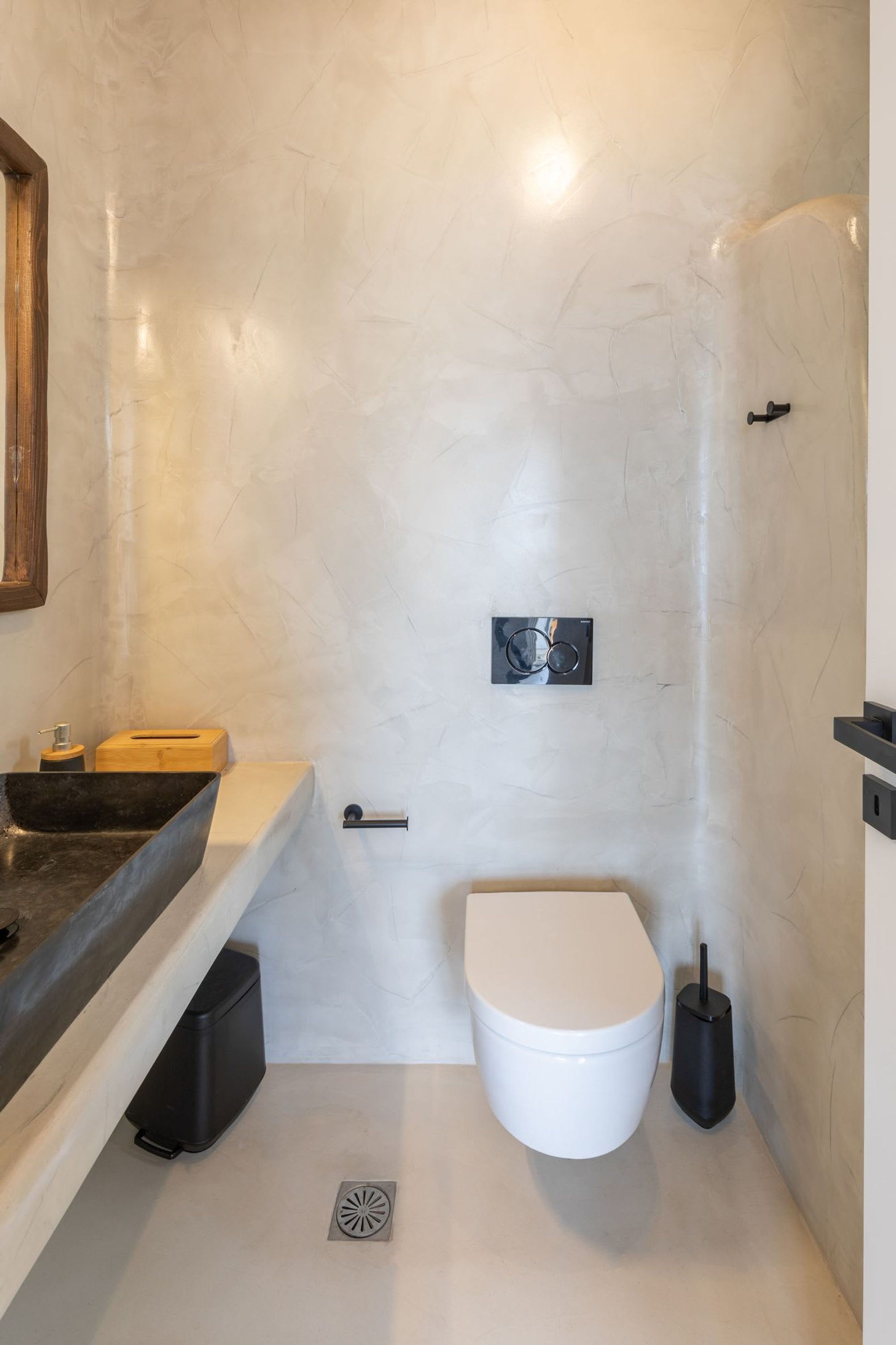 A compact bathroom with a white marble wall, a black sink, a white toilet, and a black bidet.