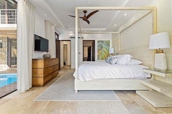 Un dormitorio moderno con cama, mesita de noche, lámpara, televisor y vistas a una piscina.