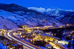 Une ville de montagne enneigée, illuminée la nuit, avec des routes et des bâtiments éclairés.