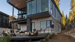 A modern two-story house with large windows, a deck with outdoor furniture, and a stone retaining wall. - Modern Ski In Out Home Mid-mountain Northstar (Truckee)