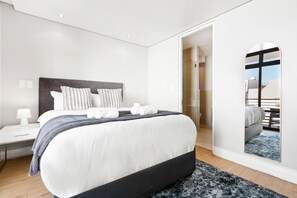 Quarto de hotel moderno com uma cama grande, mesa de cabeceira, espelho e vista exterior.