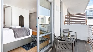 A modern bedroom with a bed, a glass door leading to a balcony, and a small table with a bottle and glasses.
