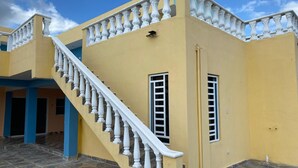 A yellow building with a white staircase and balustrade, a tiled floor, and a blue pillar.