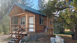 Una cabaña de madera con un porche, unos escalones y un pequeño espacio exterior con rocas.