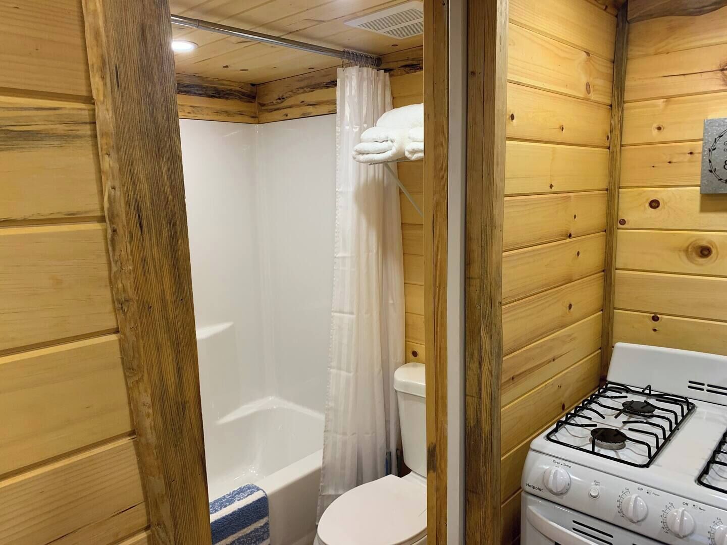 Een houten badkamer in een vakantiehuis, met een douche, toilet en een gasfornuis.