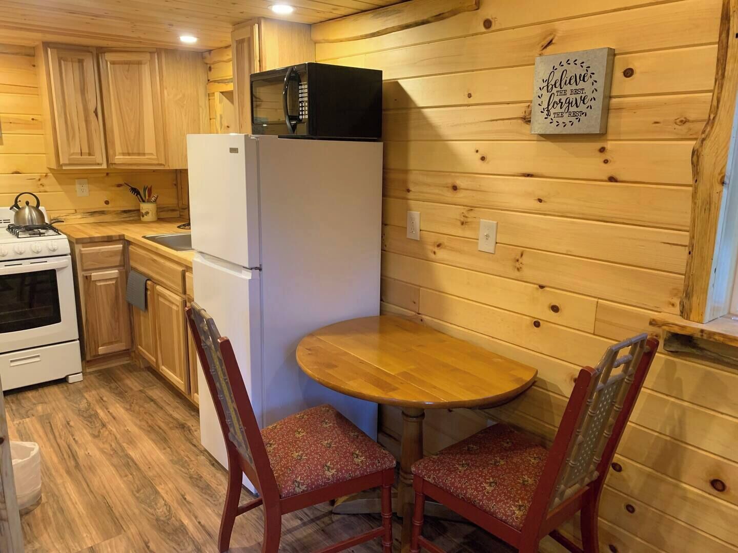 Una cocina compacta con paredes de madera, un refrigerador blanco, un microondas, una estufa y una pequeña mesa de comedor con dos sillas.