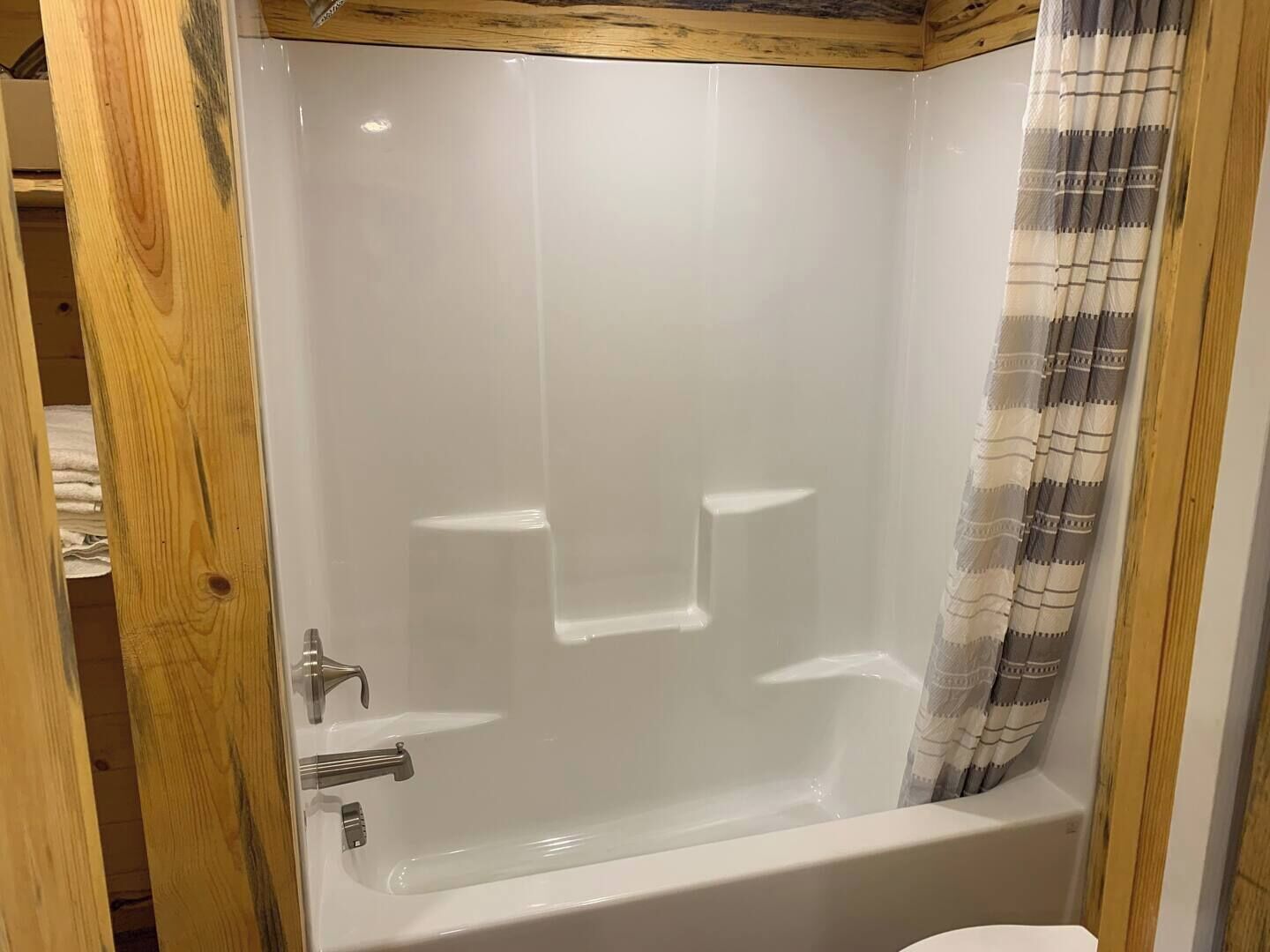 A modern bathroom with a glass-enclosed shower, a white bathtub, and a wooden ceiling.
