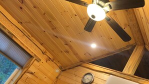 Interior de una cabaña de madera con ventilador de techo, aire acondicionado instalado, un reloj de pared y televisor.