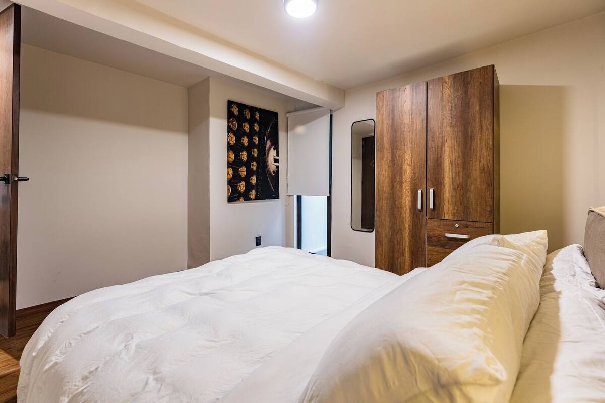 Un dormitorio con una cama grande, un armario de madera, un espejo adosado a la pared y un cuadro enmarcado.