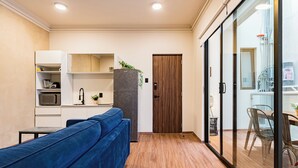A modern kitchen with white cabinets, a microwave, and a refrigerator. There is a blue sofa and a wooden door in the room.