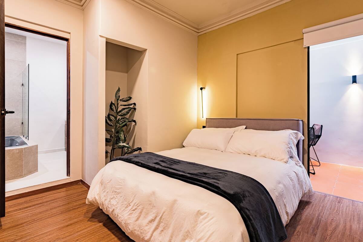Habitación de hotel con una cama grande, una planta en maceta, una mesita de noche y vistas al exterior.