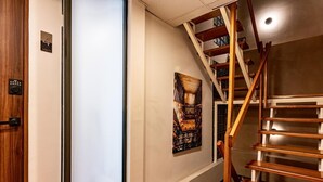 A wooden staircase with a modern design, a door with a digital lock, and a framed artwork on the wall.