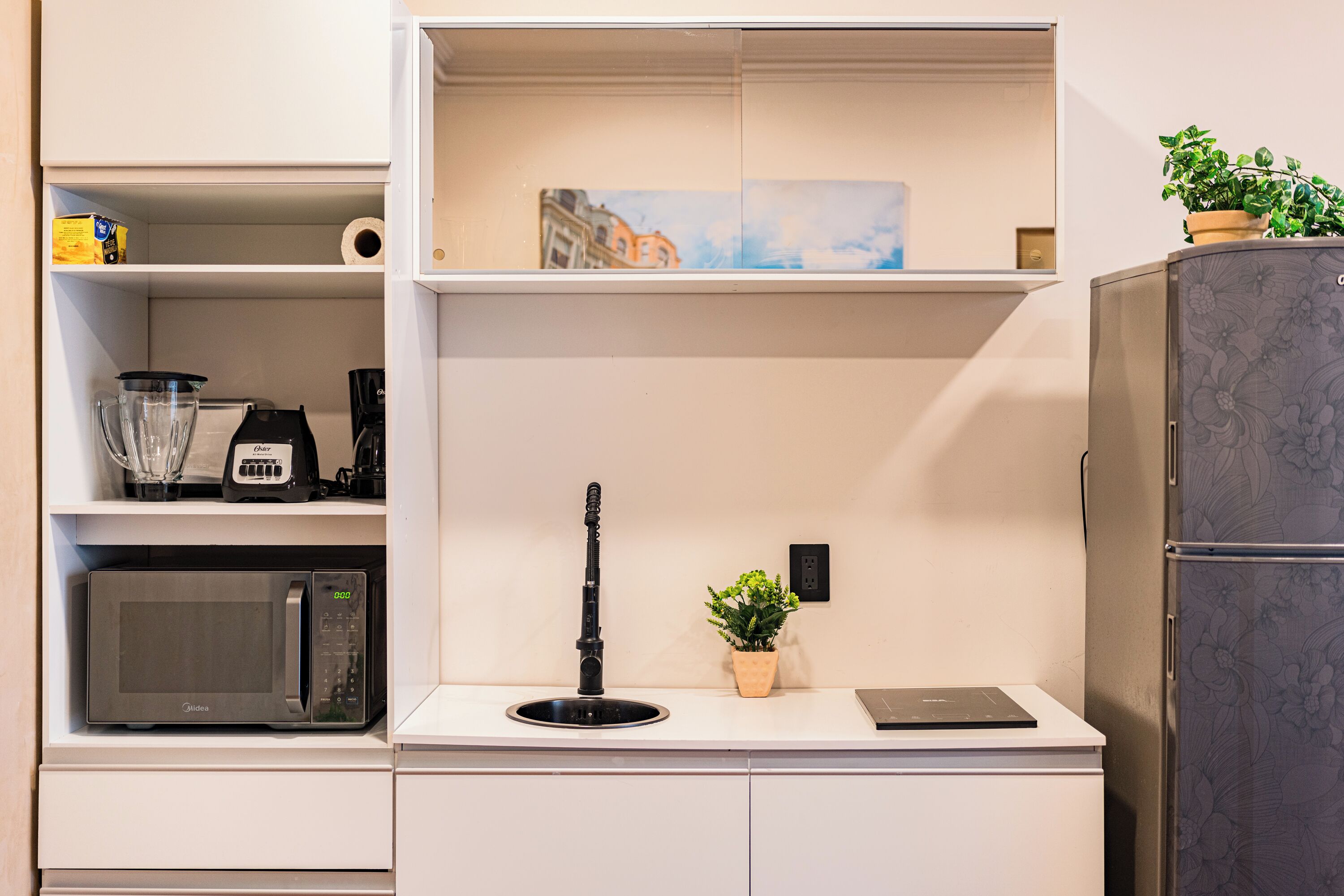 A kitchen with a microwave, a coffee maker, a blender, a kettle, and a small potted plant.