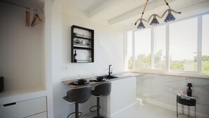 A modern kitchen with a marble countertop, black bar stools, a wine rack, and a view through large windows. - B&B LA PERLA NERA (Fasano)