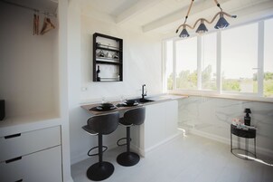 Una cucina moderna con un piano di lavoro in marmo, sgabelli da bar neri, una dispensa per vino e una vista attraverso ampie finestre.