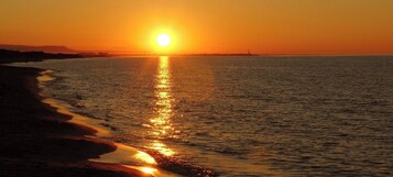 Tramonto su un mare calmo, con una spiaggia in primo piano.