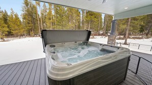 Ein Whirlpool auf einer Holzterrasse mit Blick auf eine verschneite Landschaft und Bäume.
