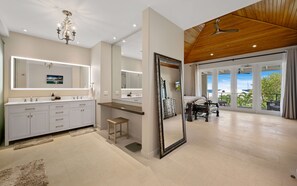 A modern bathroom with a large mirror, vanity, and a ceiling fan.