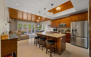 A modern kitchen with wooden cabinets, stainless steel appliances, and a large island with bar stools. - The Pirate's Landing North - St. John USVI - Chocolate Hole (Cruz Bay)