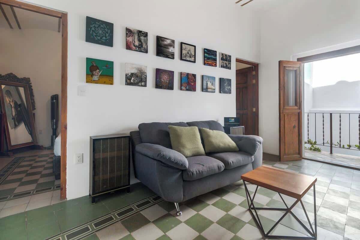 A living room with a grey sofa, a small wooden table, and a wall adorned with various framed artworks.
