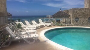 A pool area with lounge chairs and a view of the ocean. - Columbus Heights Apts  (Ocho Rios)