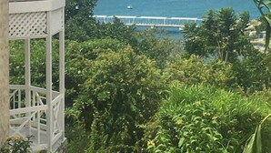 A view of a coastal area with a white gazebo, lush greenery, and a clear blue sea with boats and a bridge in the distance. - Columbus Heights Apts  (Ocho Rios)