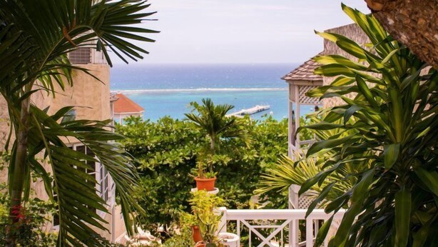 A view of a coastal area with a building, palm trees, and a boat on the water. - Columbus Heights Apts  (Ocho Rios)