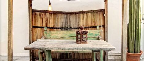 A rustic outdoor seating area with a wooden table, two stools, a lantern, and a cactus plant.