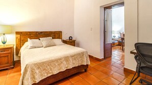 A bedroom with a wooden bed, a nightstand with a lamp, a chair, and a view of a balcony through an open door.