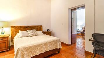 A bedroom with a wooden bed, a nightstand with a lamp, a chair, and a view of a balcony through an open door.