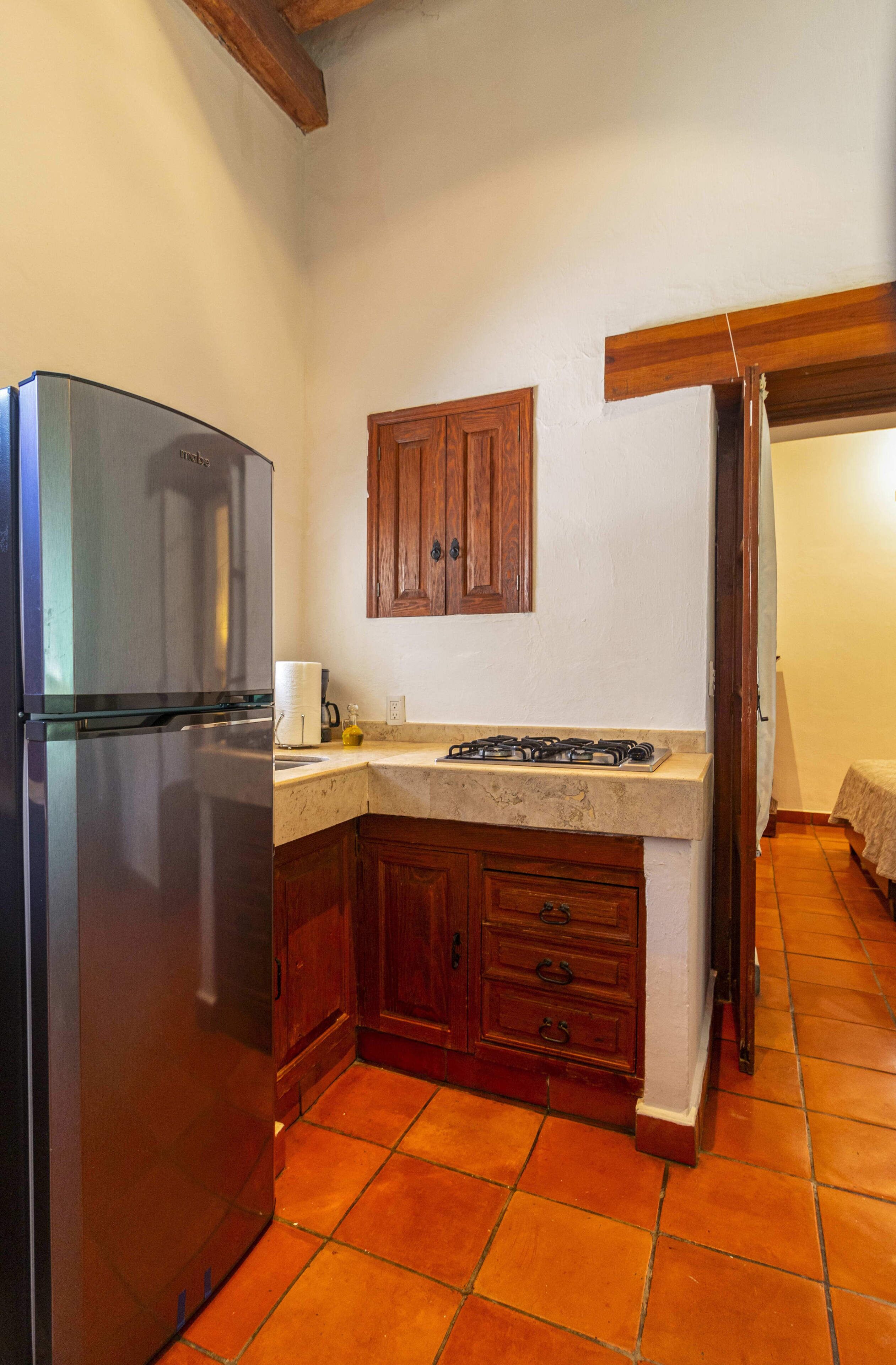 A kitchen with a stainless steel refrigerator, wooden cabinets, a countertop, and a tiled floor.