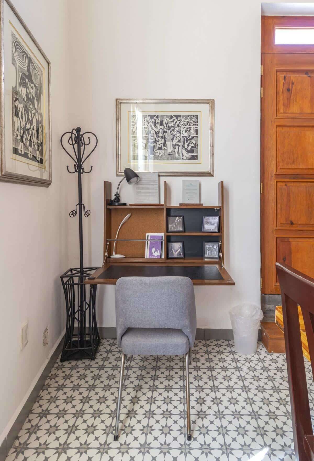 A study with a desk, chair, framed artwork, and a bookshelf.