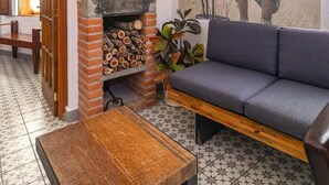 Une pièce avec une cheminée en briques, un canapé, une table en bois et une fresque représentant une personne tenant un chat.