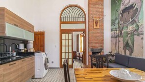 Une cuisine équipée d’un lave-linge, une table à manger avec un saladier, un canapé et une fresque murale.