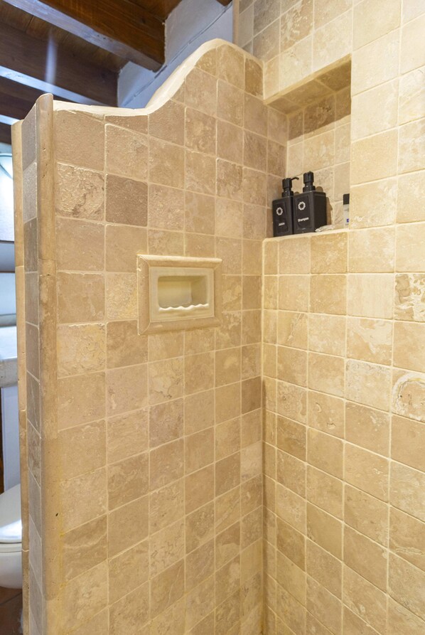A corner of a room with beige tiled walls and a recessed shelf with toiletries.
