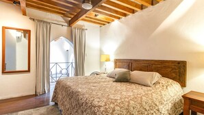Een slaapkamer met een houten plafond, een bed met beddengoed met een patroon, een nachtkastje en een raam met gordijnen.