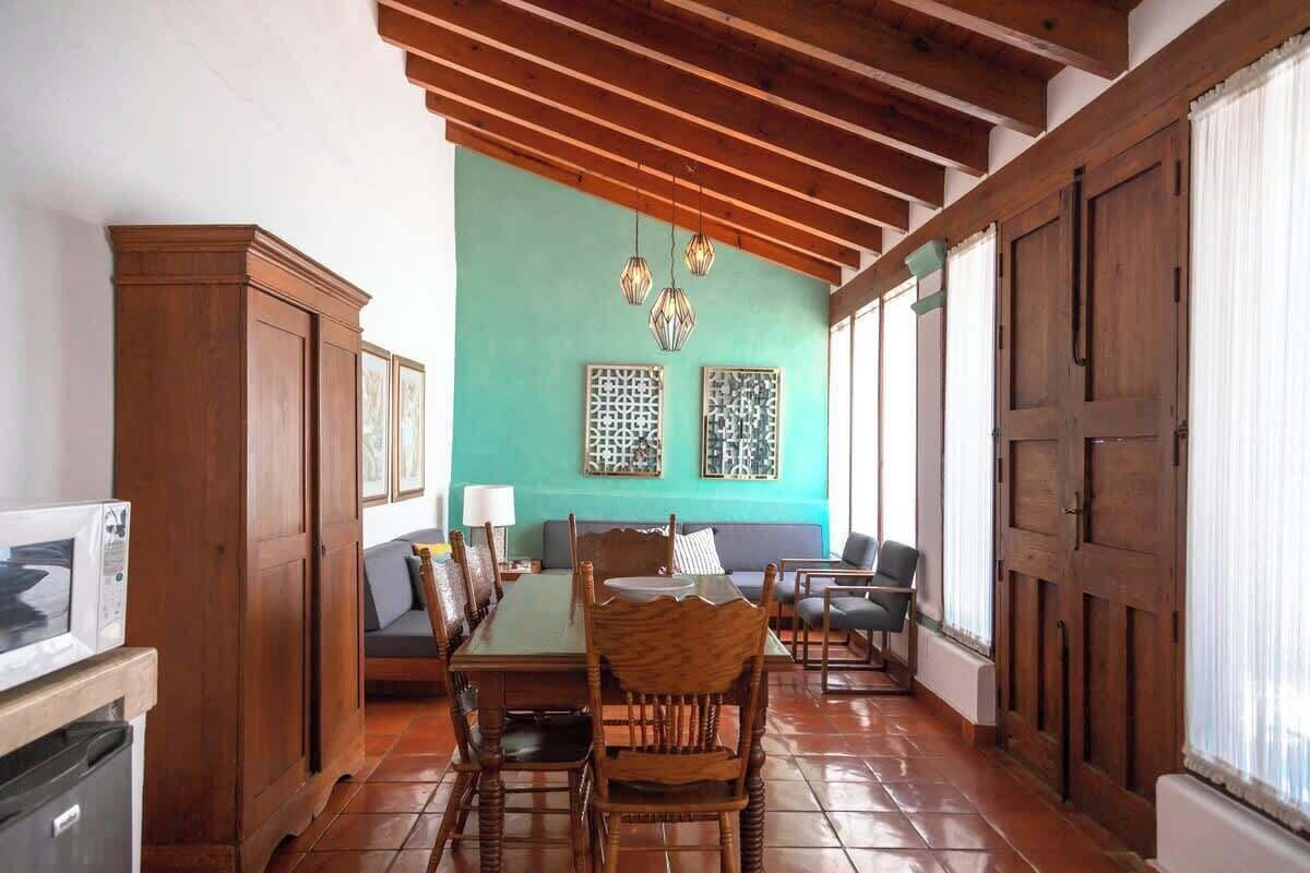 A dining area with a wooden table and chairs, a sofa, and a kitchen area with cabinets and a microwave.