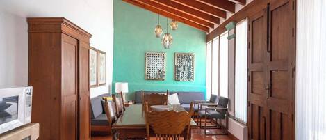 A dining area with a wooden table and chairs, a sofa, and a kitchen area with cabinets and a microwave.
