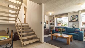 A staircase leading to an upper floor, a dining area with a table and chairs, a living room with a sofa and a coffee table, and a bookshelf with various items. - Huge apartment, top location w/terrace. 4bd 3.5ba (Santiago de Querétaro)