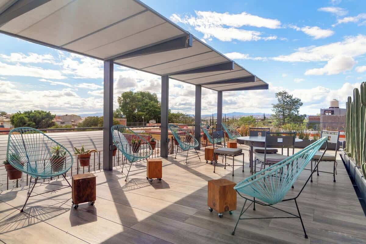 Un patio al aire libre con sillas y mesas de metal, y plantas en macetas.