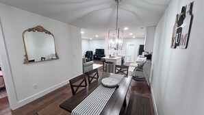 Een moderne woonkamer met een eethoek, een grote spiegel en een keuken op de achtergrond.