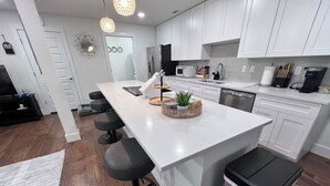 Een moderne keuken met witte kasten, een groot eiland met barstoelen, een magnetron en een vaatwasser.