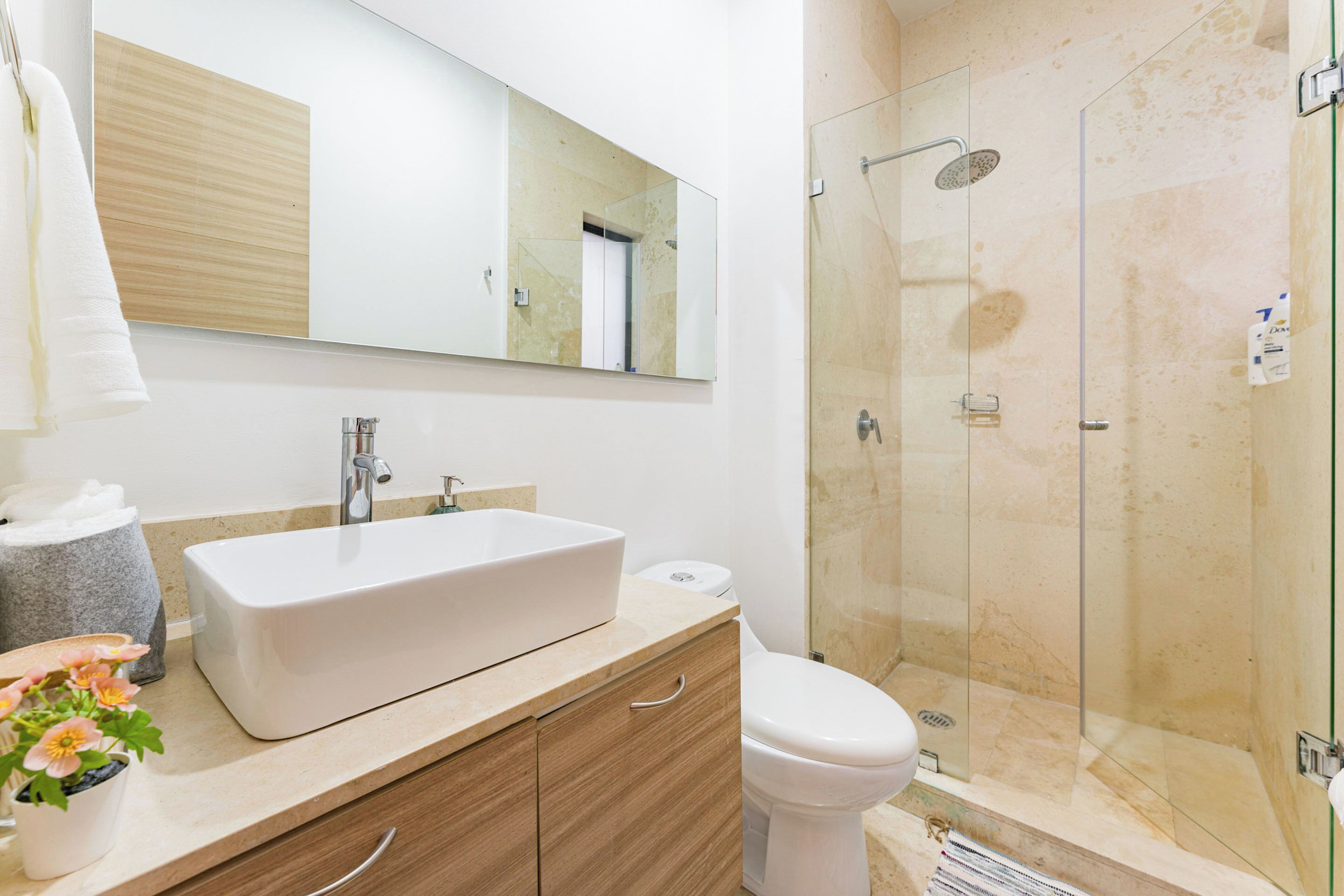 A modern bathroom with a large mirror, a white sink, a toilet, and a glass-enclosed shower.