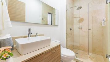 A modern bathroom with a large mirror, a white sink, a toilet, and a glass-enclosed shower.