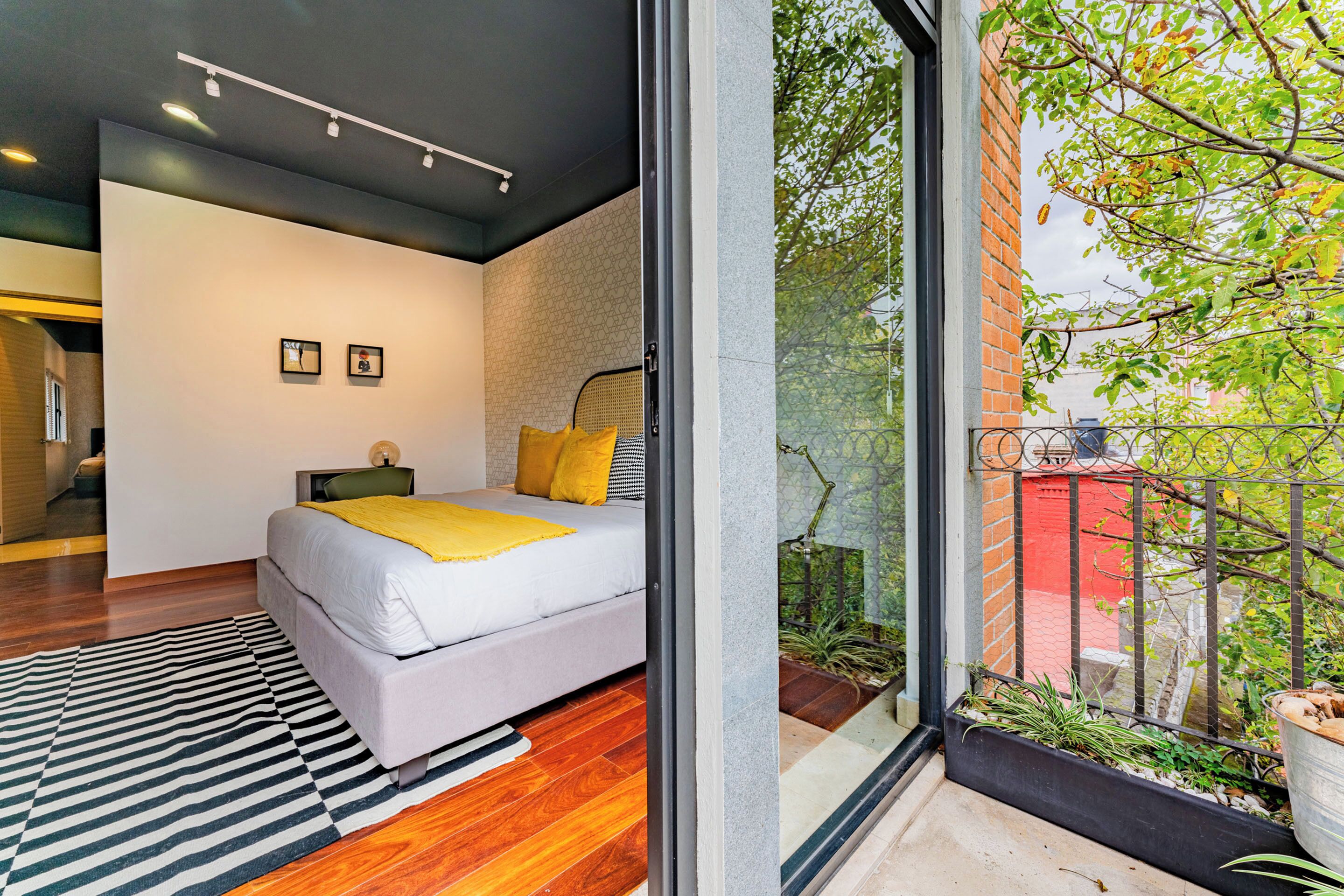 A modern bedroom with a large bed, a black and white striped rug, and a view of a garden through a glass door.