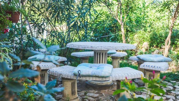 A stone outdoor seating area with multiple tables and benches, surrounded by lush greenery and a stone pathway. - Apartments Jug - Studio Apartment with Private Garden (Lopar)