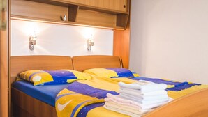 A double bed with a colorful quilt, wooden headboard, and two wall-mounted lights. - Apartments Jug - Studio Apartment with Private Garden (Lopar)