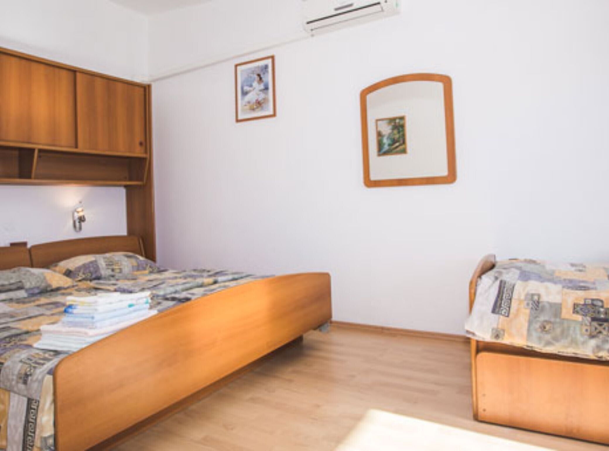 A bedroom with a wooden bed, a wooden wardrobe, and two framed pictures on the wall.