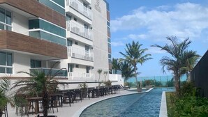 A modern hotel with a pool, outdoor seating, and palm trees. - Pé na Areia em Ponta de Campina, Paraíba (Cabedelo)